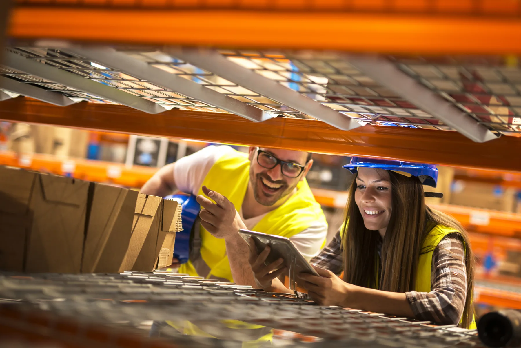 Warehouse workers using a tablet to review stock on industrial shelving